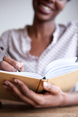 Partial portrait of smiling black female author at home writing in notebook