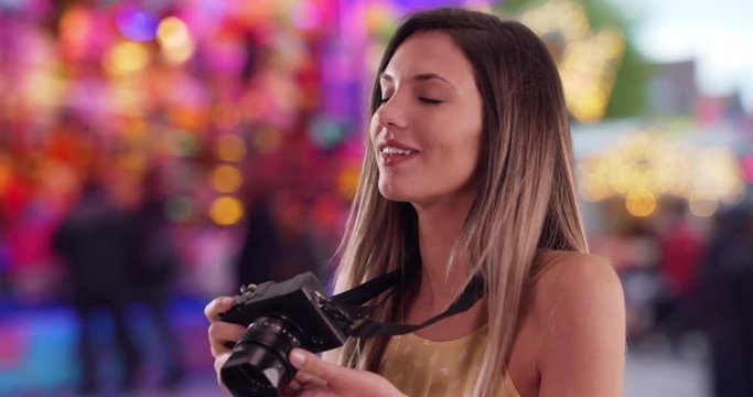 Happy Caucasian woman with camera taking photos outside at festive street fair, Brunette millennial in her 20s shooting pictures with camera at street carnival, 4k