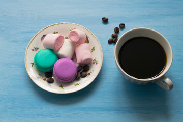 Cup of hot coffee with marshmallows and macaroons on blue background.