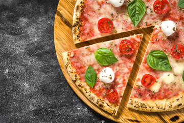 Italian pizza slice with tomatoes, cheese and basil on black stone. Top view. Copyspace