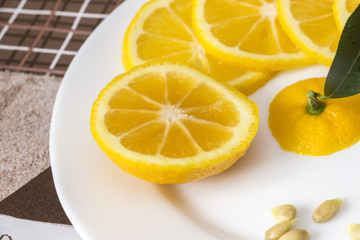 Sliced orange-yellow lemon of Volkamer with a small green leaf and seeds on a white plate, indoor culture of growing citrus plants, close-up
