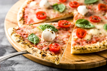 Italian pizza slice with tomatoes, cheese and basil on black stone. 