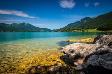 See in Österreich welcher Wolfgangsee genannt wird mit Berge im Hintergrund und Wolken am Himmel und im Vordergrund Steine im Wasser