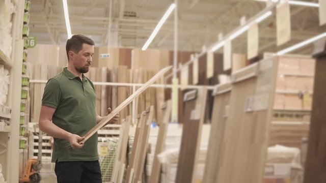 Adult man is holding a parquet deck in a building store. Man looking for new supplies to renovate the house. Customer in a store.