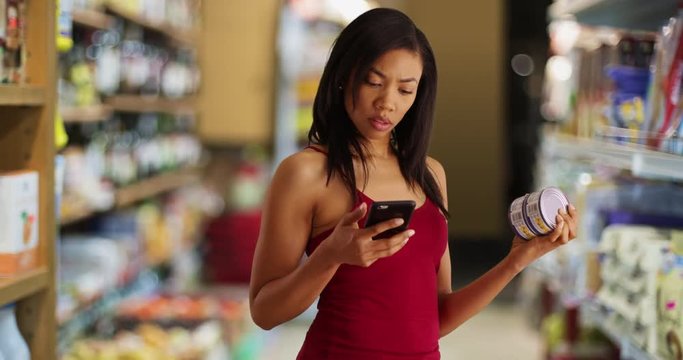 Black woman at the grocery store taking picture of canned tuna info label with cellphone, Young female on a diet checking nutritional facts of food product using mobile app, 4k