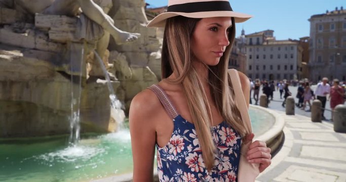 Pretty lady in floral romper wearing fedora and holding bag by Fiumi Fountain in Rome, Stylish young woman in her 20s in summer dress by fountain in Rome, Italy, 4k
