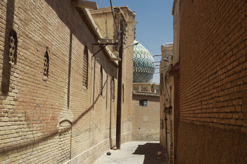 wąska uliczka w arabskim kraju z domami i ozdobną kopułą meczetu w tle