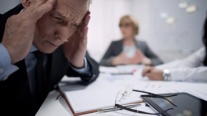 Man holding his head, migraine attack caused by stress, exhaustion at workplace