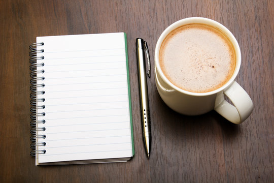 Blank notebook, pen and cup of coffee on wooden brown background, copy space.