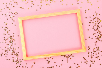 A wooden empty frame on a pastel background surrounded by shiny decorative stars and balls.