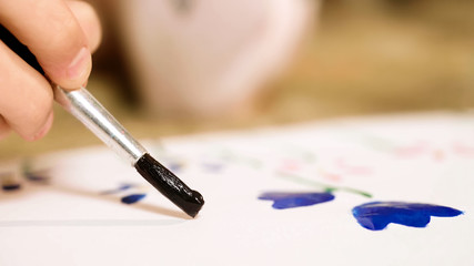 Closeup of child hand carefully drawing flowers with gouache, creativity, talent