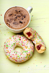 Cup of coffee and tasty donuts with icing and chocolate on green wooden background, copy space