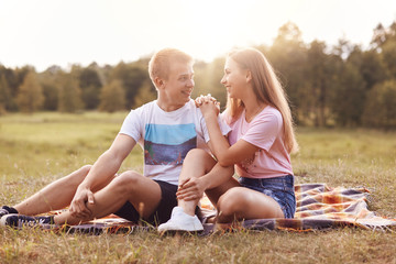 Horizontal portrait of happy boyfriend looks with great love at her girlfriend, have date outdoor, demonstrate truthful feeling, spend free time during summer vacation. People and lifestyle concept