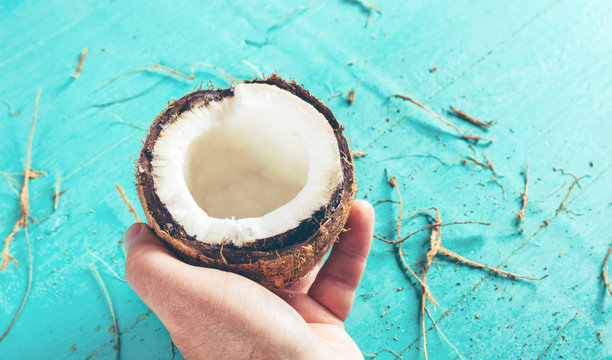 Half of a chopped coconut in a hand on a blue background with a peel