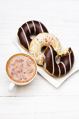 Cup of coffee and tasty donuts with icing and chocolate on white wooden background, copy space