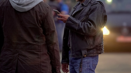 Two men in jackets order taxi outdoor, waiting for cab driver to pick them up