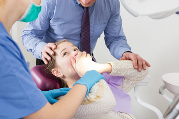 Frightened girl in dental chair refusing to open mouth