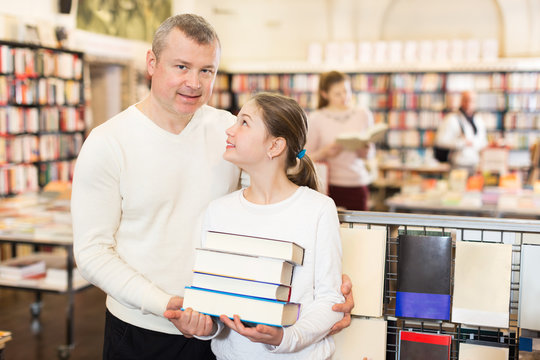 Girl with father standing with books in bookshop