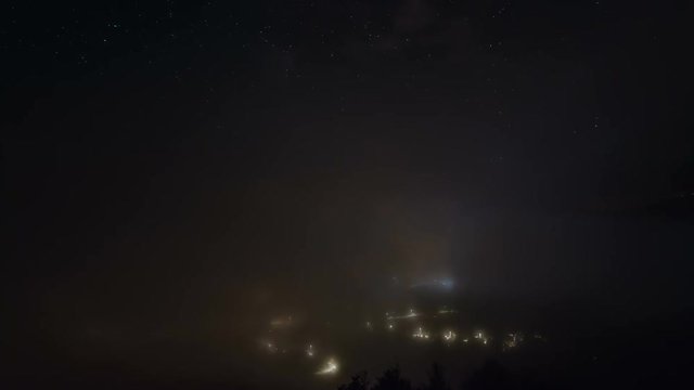 Stars with milky way and waves of misty clouds over night village Time lapse