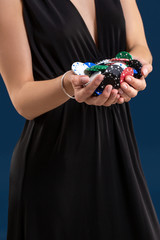 Elegant female casino player holding a handful of chips on dark blue background, hands close up