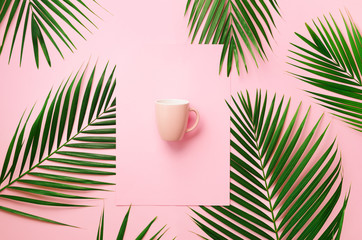 Tropical palm leaves on pastel pink background with paper card note, cup. Minimal summer concept. Creative layout. Top view, flat lay. Green leaf on punchy pastel paper