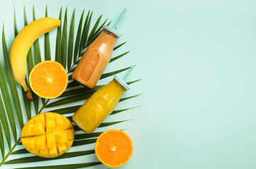 Fresh orange, banana, pineapple, mango smoothie and juicy fruits on palm leaves over blue...