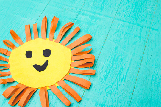 Children's handmade from colored paper - the sun with a smile on blue background