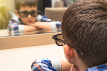 Little boy with glasses looks at himself in the mirror