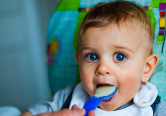 baby boy eating food with spoon at home