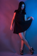 A young girl in a black dress stands on a blue-pink background