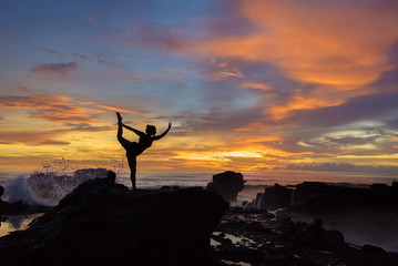 silhouette of a girl practicing yoga at sunset on a background of waves