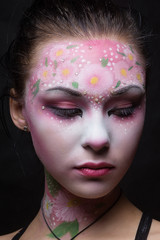 Portrait of a cute girl with flowers body art on her face on a black background