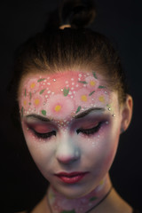 Portrait of a cute girl with flowers body art on her face on a black background