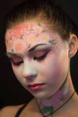 Portrait of a cute girl with flowers body art on her face on a black background