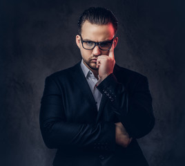 Close-up portrait of a thoughtful stylish businessman with serious face in an elegant formal suit and glasses on a dark background.