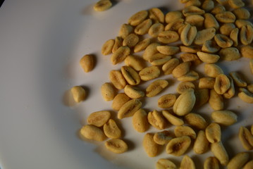 On white glass plate are peanut nuts with salt fried in yellow earth-nut, groundnut, goober, monkeynut