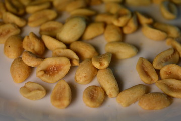 On white glass plate are peanut nuts with salt fried in yellow earth-nut, groundnut, goober, monkeynut