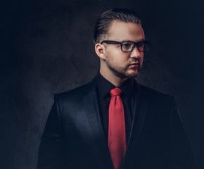Portrait of a mystical stylish male in a black suit and red tie. Isolated on a dark background. 