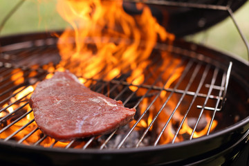 Tasty meat on barbecue grill with fire flames outdoors, closeup