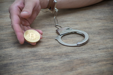 Hand in handcuffs holding bitcoin. Closeup