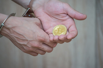 Hand in handcuffs holding bitcoin. Closeup