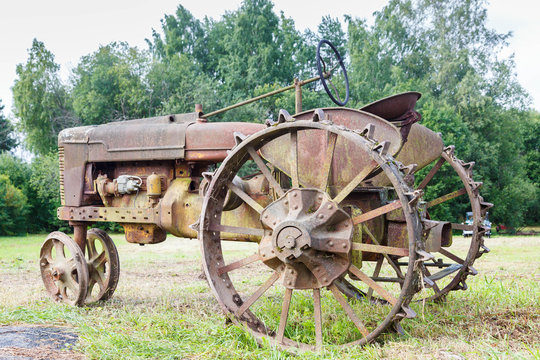 Very old rusted tractor sitting in a green field under a bright blue sky in the summer time - Powered by Adobe