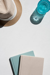 Flat lay of straw sun hat with books and a glass of water