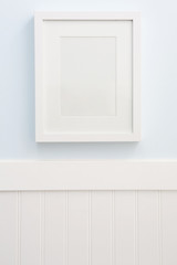 White frame mockup hanging on a blue wall with white wainscoting.