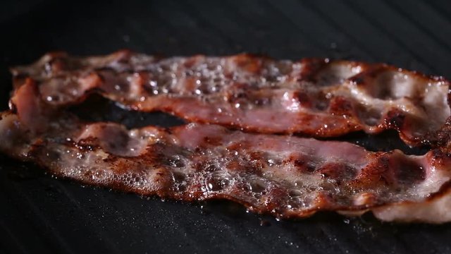 Close Up View Of Two Slices Of Bacon Frying On Grill Pan
