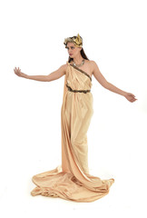 full length portrait of brunette woman wearing long golden grecian gown, standing pose. isolated on white studio background.