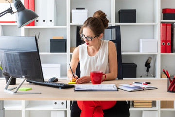 A young girl sits at a table in her office, holds a pencil in her hands and writes them on a sticker.