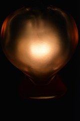 A glass bottle in the shape of a heart on the matt interior with illumination of the candle, art color