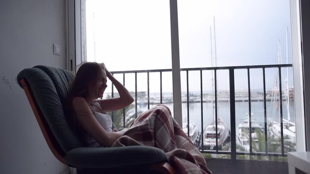 Young depressed woman suffering a distress sitting in chair by the window with the sea view. Raining outside. Lonely woman in despair.