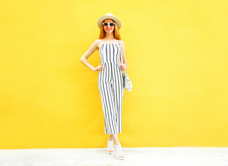 Fashion smiling woman is wearing a white striped pants, round hat posing on colorful yellow...